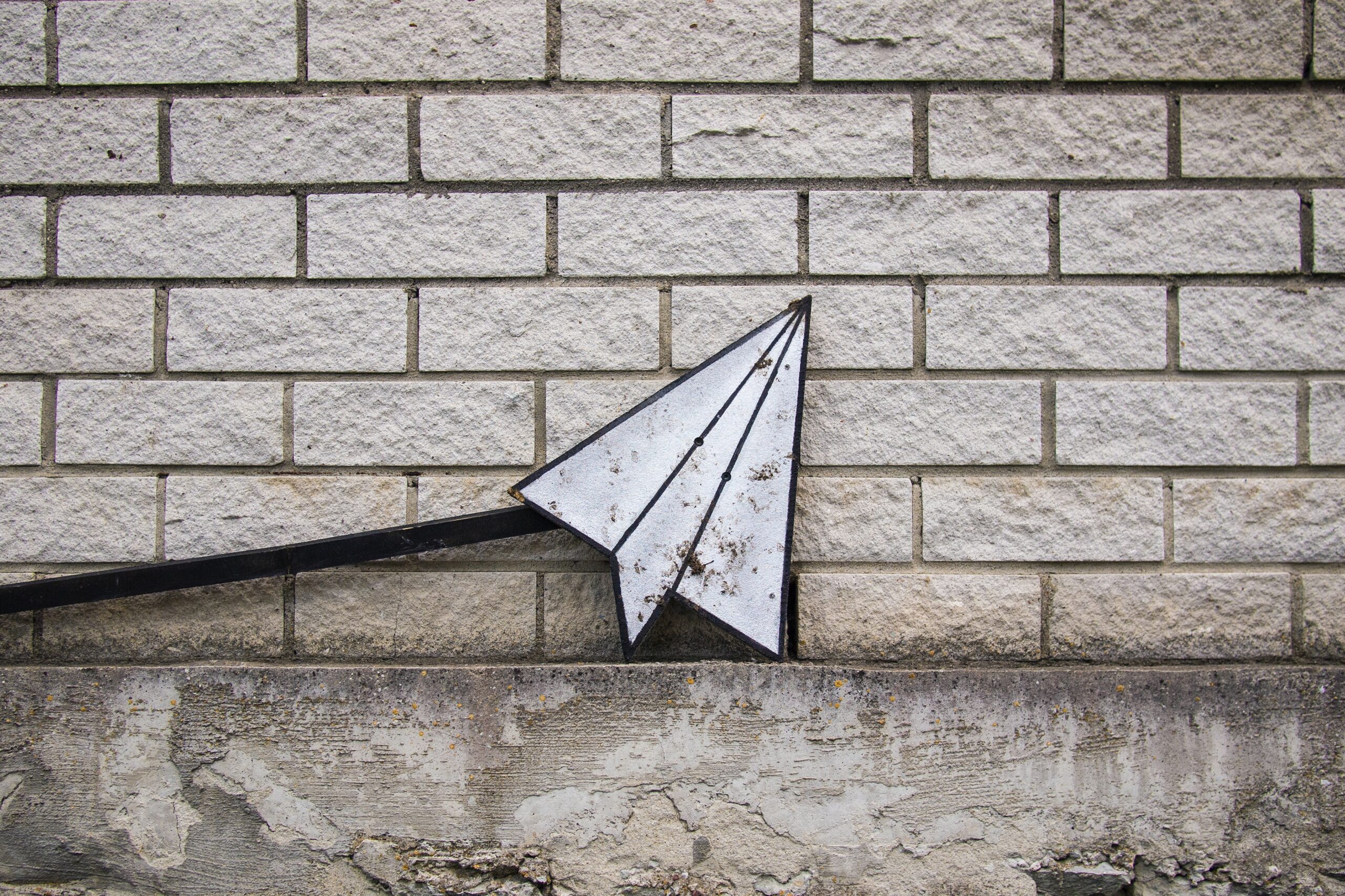 A paper aeroplane in front of a brick wall