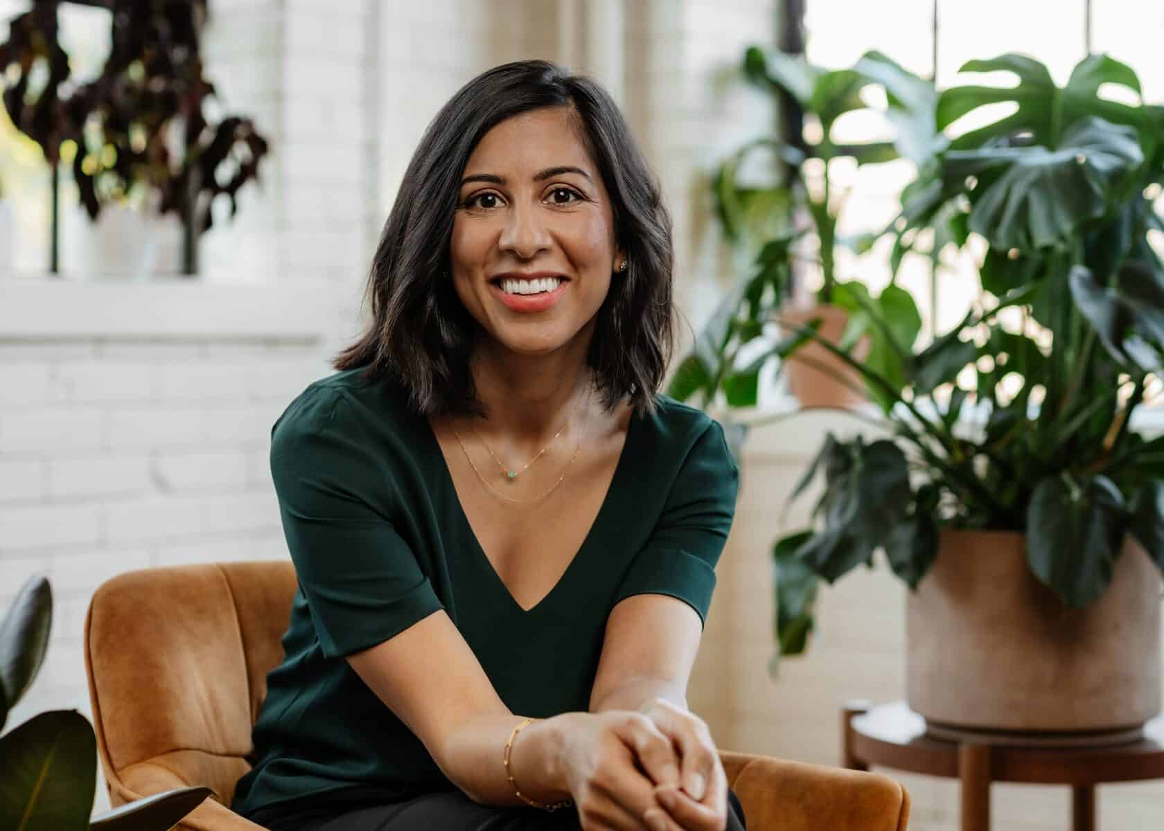 woman smiling and sitting on a brown chair with plants in the background