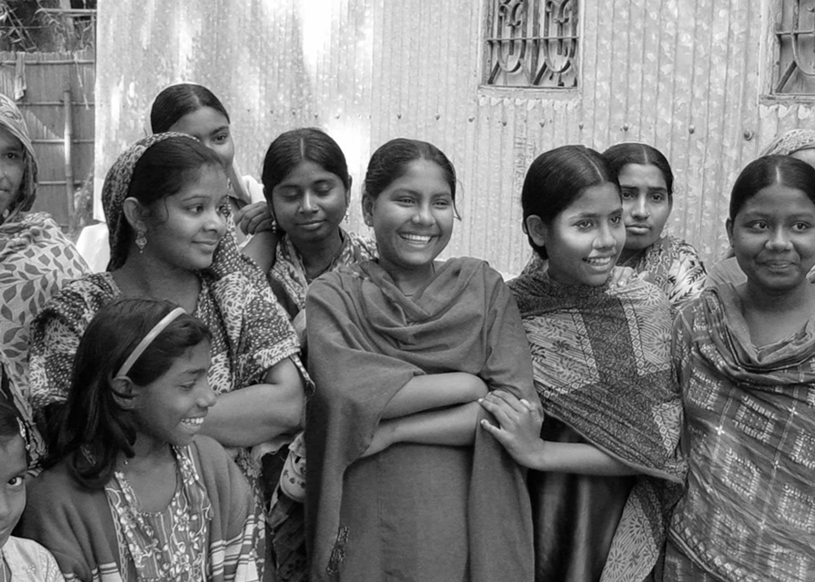 A black and white image of nine girls wearing saris, standing close together and looking off camera