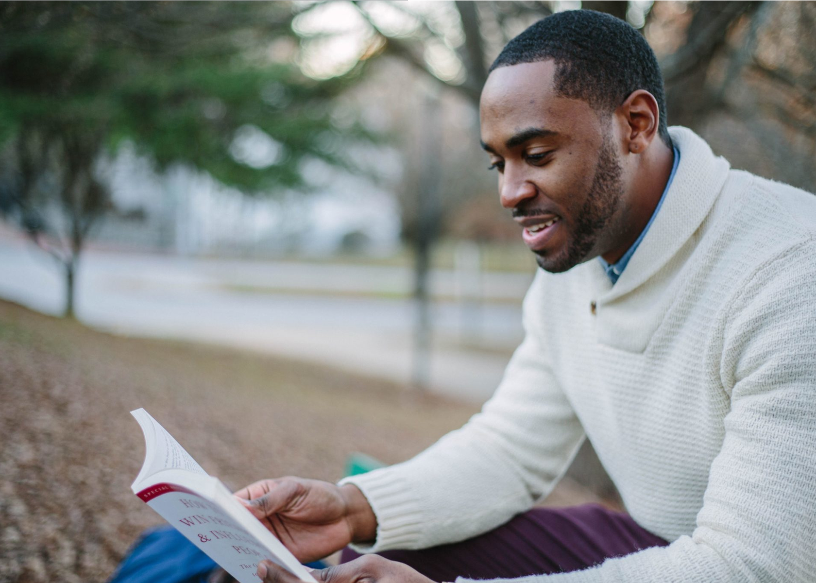 A man sits outside reading a book and smiling