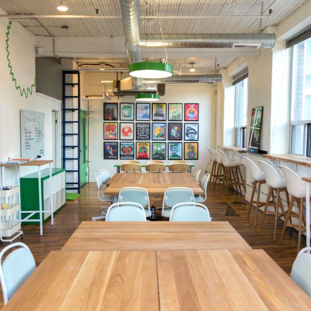 A bright and colorful office space with wooden desks, exposed ceilings and colorful artwork on the wall