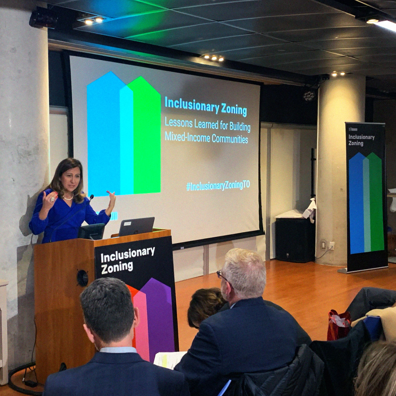 A woman stands in front of a screen and gives a presentation to a seated audience