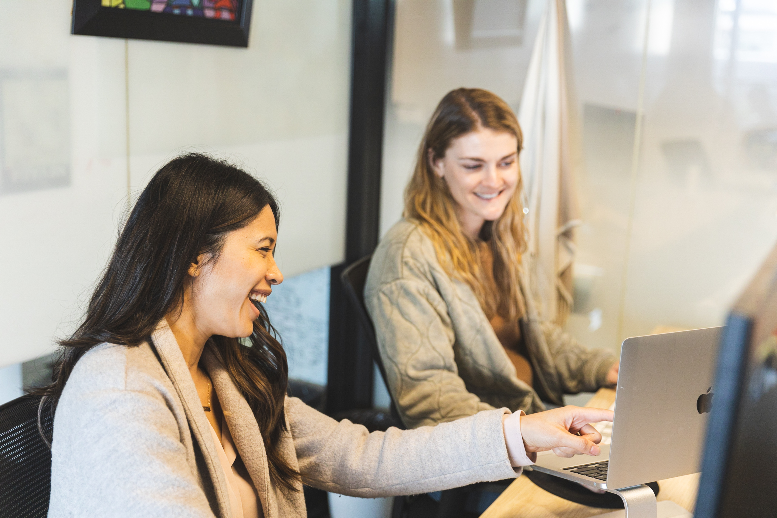 Two women smiling and working together in an office