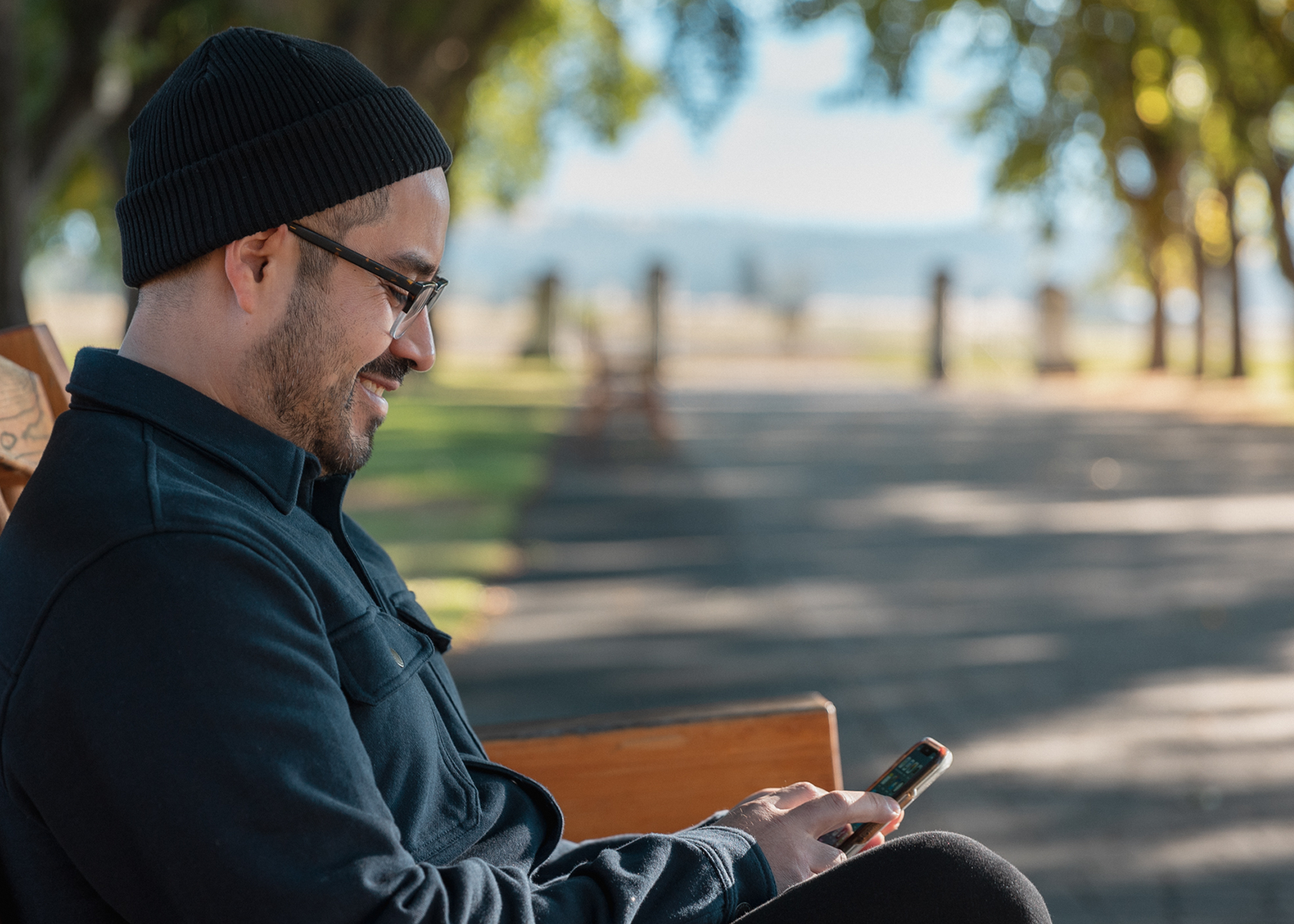 A man sits on a bench and looks at his phone smiling