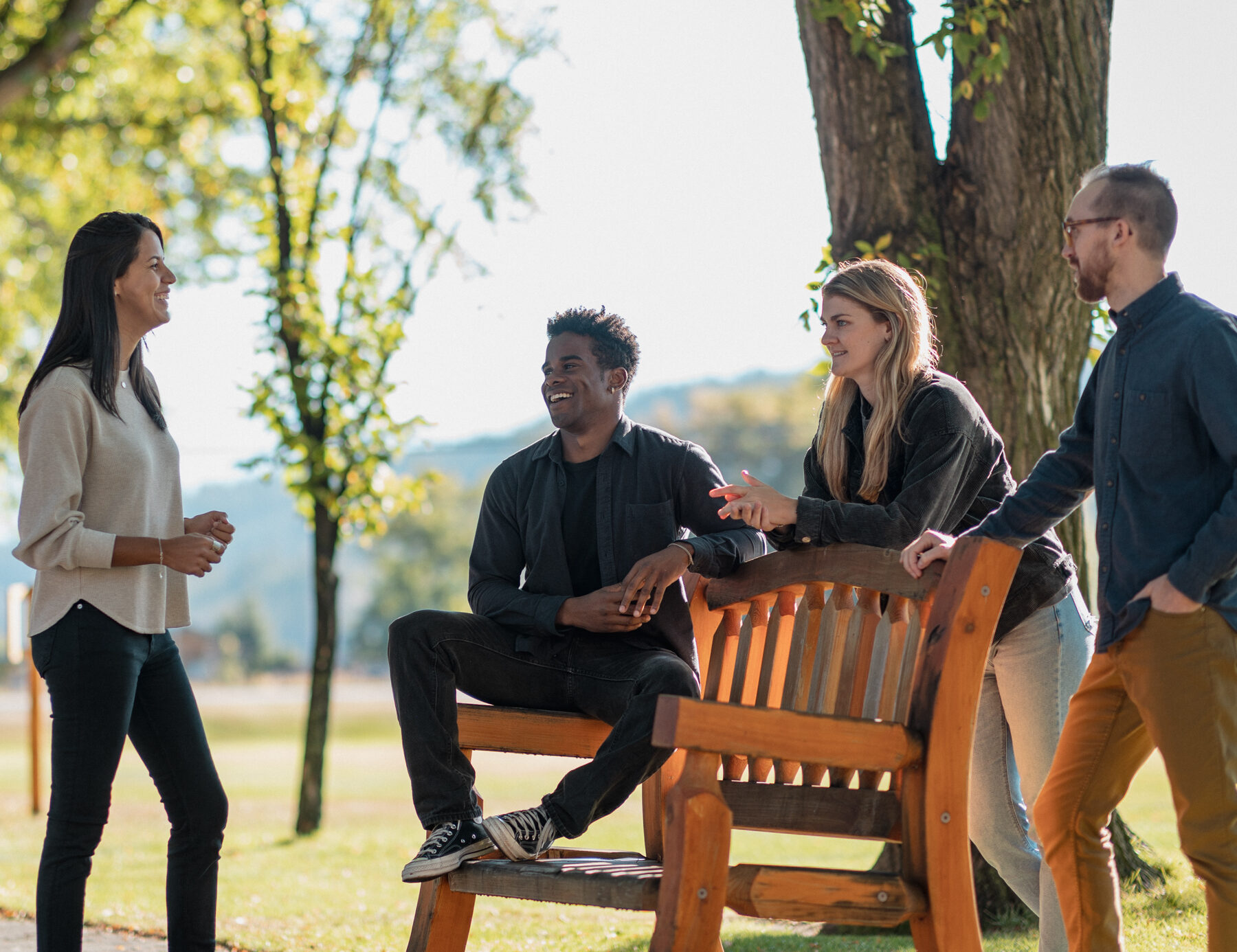 Four people talk together around a bench outside