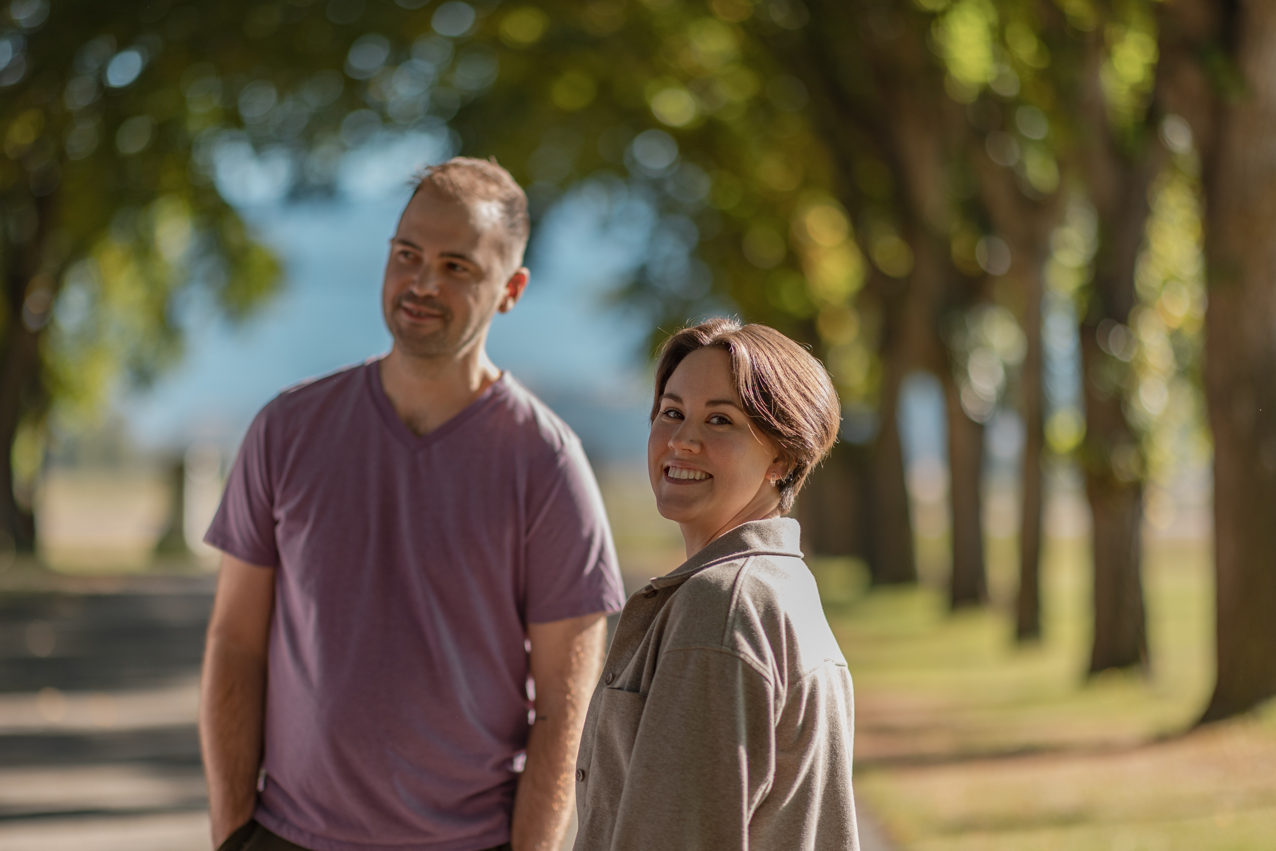 Two people stand next to trees smiling